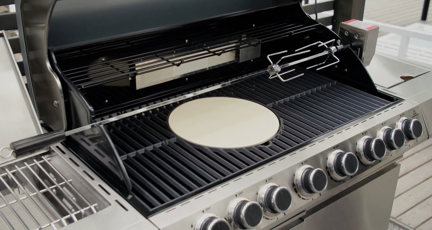 Avattu ruostumaton teräksinen kaasugrilli, mustat ritilät ja vaalea pizzakivi keskellä