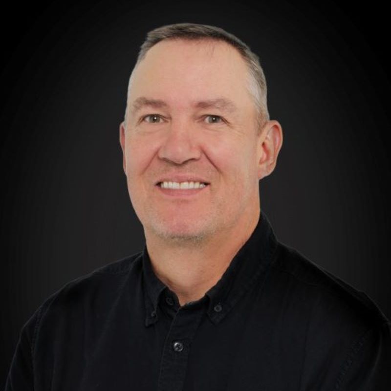 Lyhythiuksinen henkilö mustassa kauluspaidassa tummanharmaalla taustalla