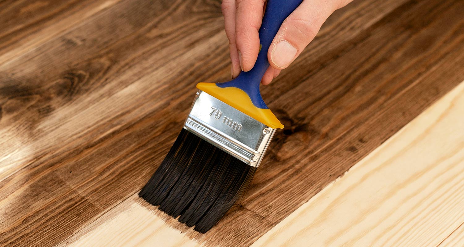 Käsi maalaa puulautaa tummaksi sinikeltaisella 70 mm pensselillä.