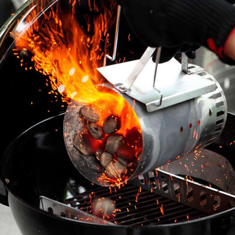 Kädessä suojahansikkaassa sytytyskartio valuttaa kipinöiviä, hehkuvia grillihiiliä