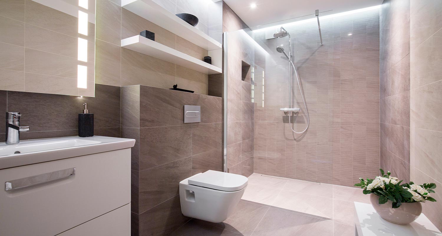 Vaalea beige-harmaa kylpyhuone, lasiseinäinen suihku, valkoinen pesuallas, pönttö ja viherkasvi