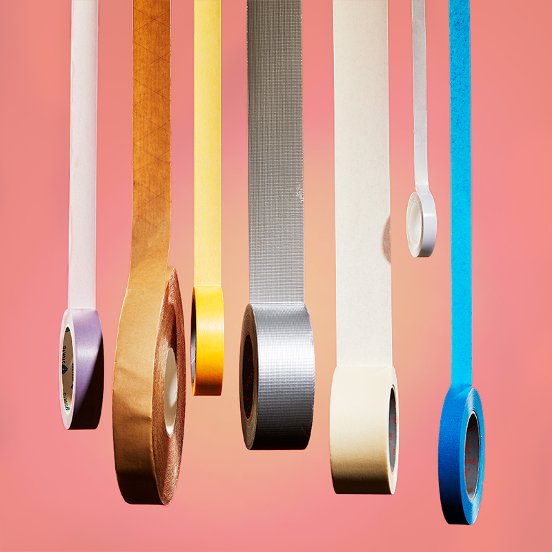 Seinältä roikkuvia eri värisiä teipinauhoja pastellipinkkiä taustaa vasten.