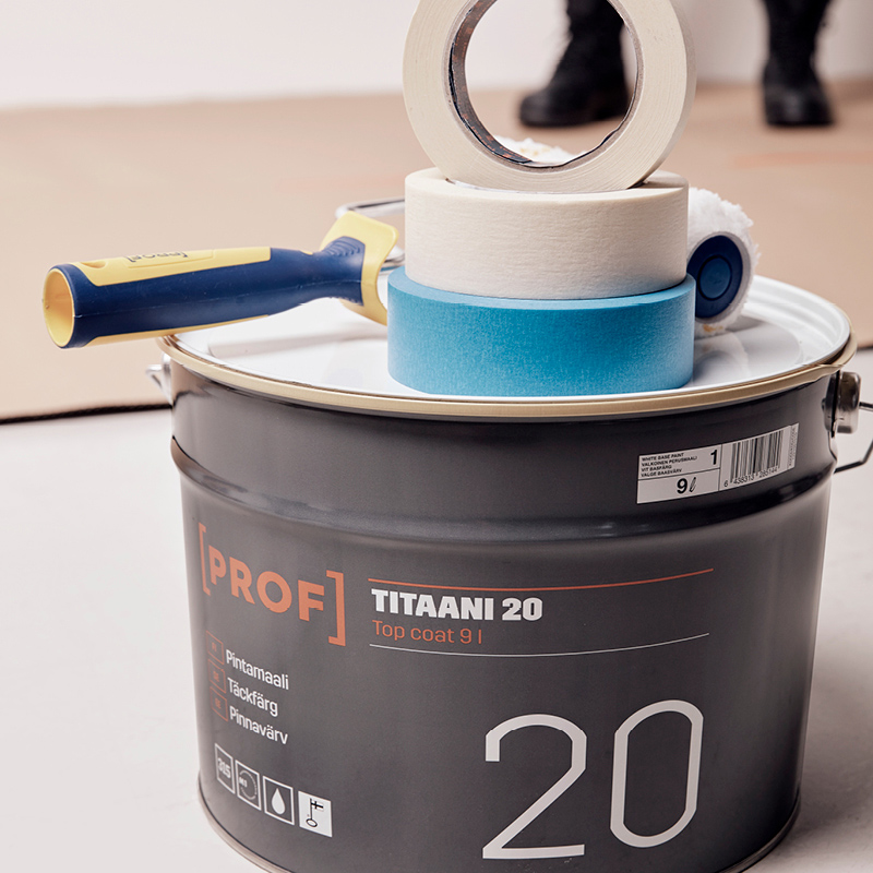 Musta PROF TITAANI 20 -maalipurkki, päällä sininen ja beige maalarinteippi sekä valkoinen tela.