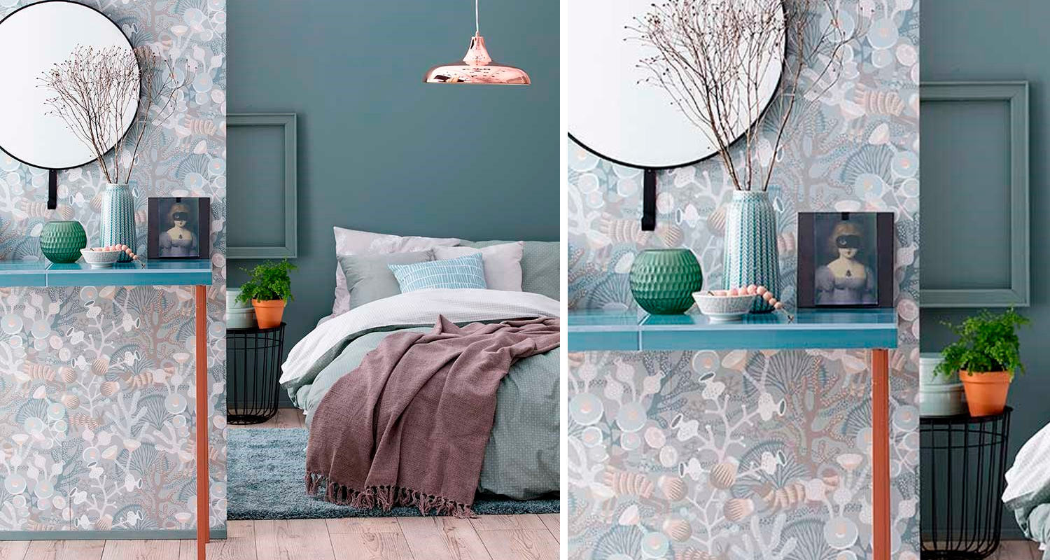 Makuuhuone, siniharmaa seinä, pastellisängynpeite, kuviotapetti ja turkoosi taso maljakoineen