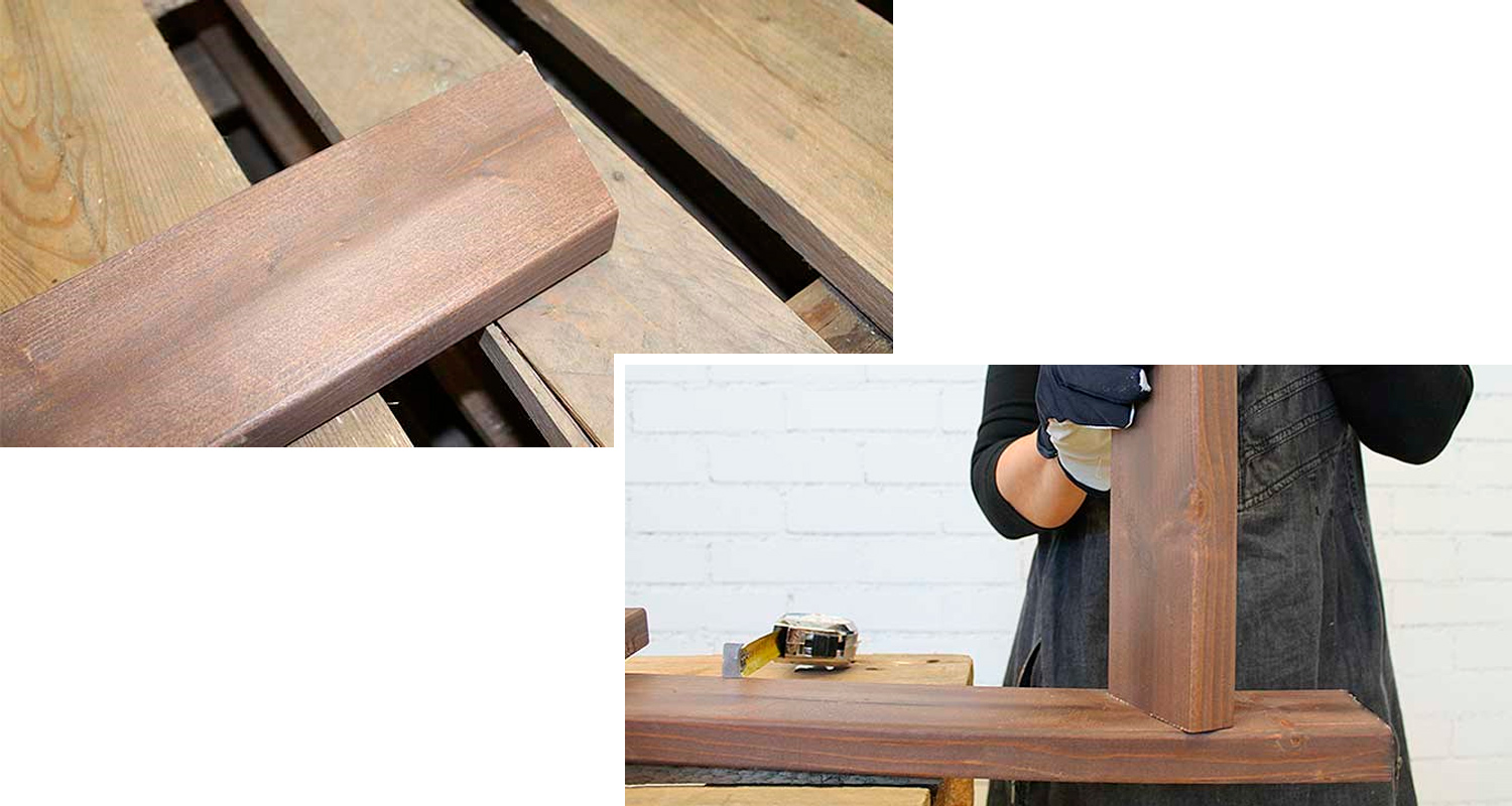 Käsineet pitävät ruskeaa L-muotoista puulautaa valkoista tiiliseinää vasten.