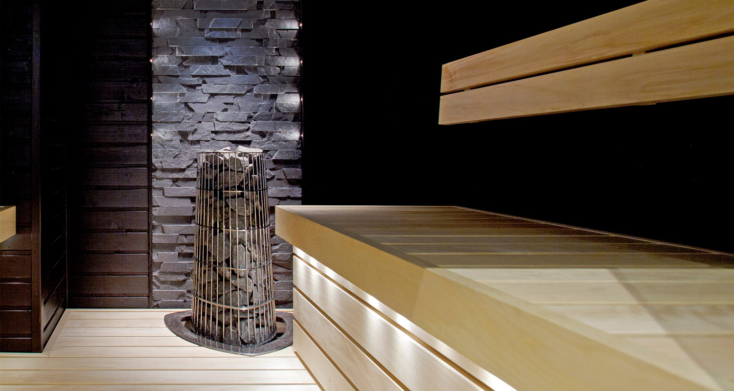 Moderni sauna: vaaleat lauteet, tumma kiviseinä ja metallikehystetty kiuaskasa