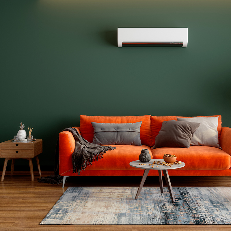 Oranssi sohva harmaine tyynyineen ja pieni pöytä, tumma vihreä seinä, valkoinen ilmastointilaite.