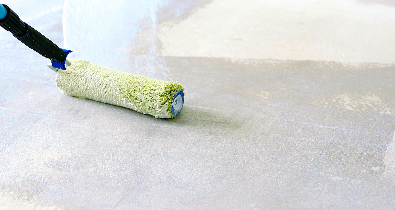 Maalausrulla levittää vaaleanvihreää maalia harmaalle pinnalle, musta-sinisellä kahvalla