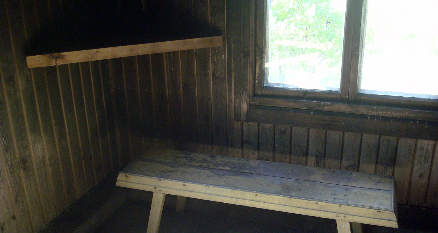 Vanha harmaa puupenkki tummassa lautarakenteisessa huoneessa ikkunan vieressä