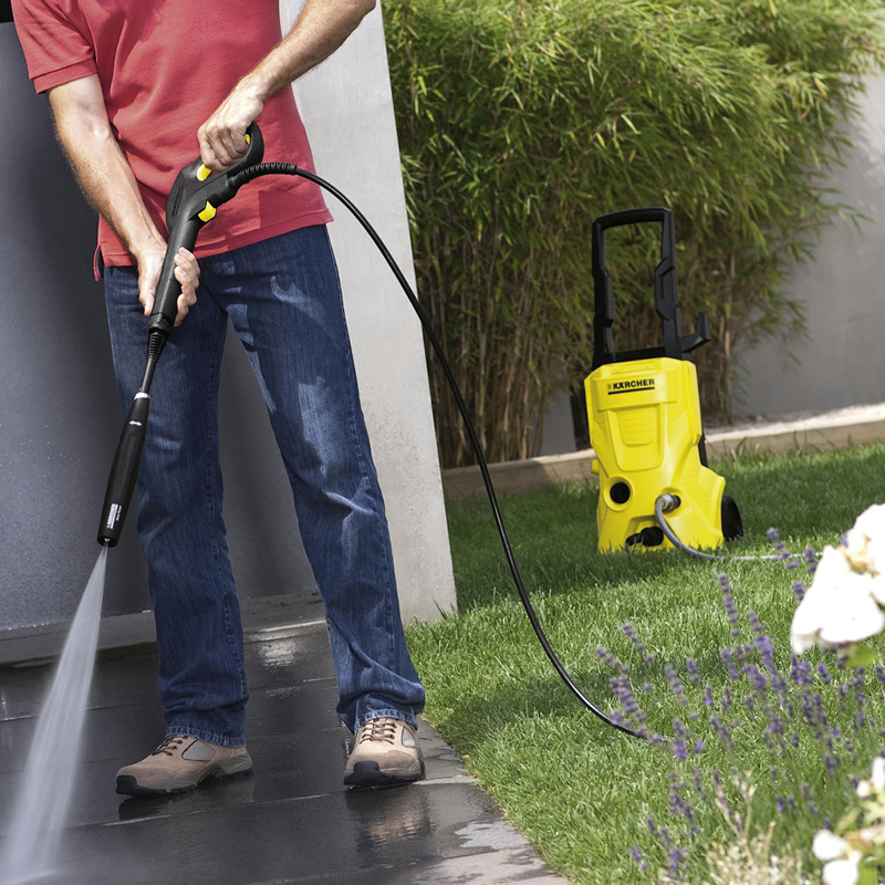 Mies pesee pihalaattaa keltaisella Kärcher-painepesurilla nurmikolla.