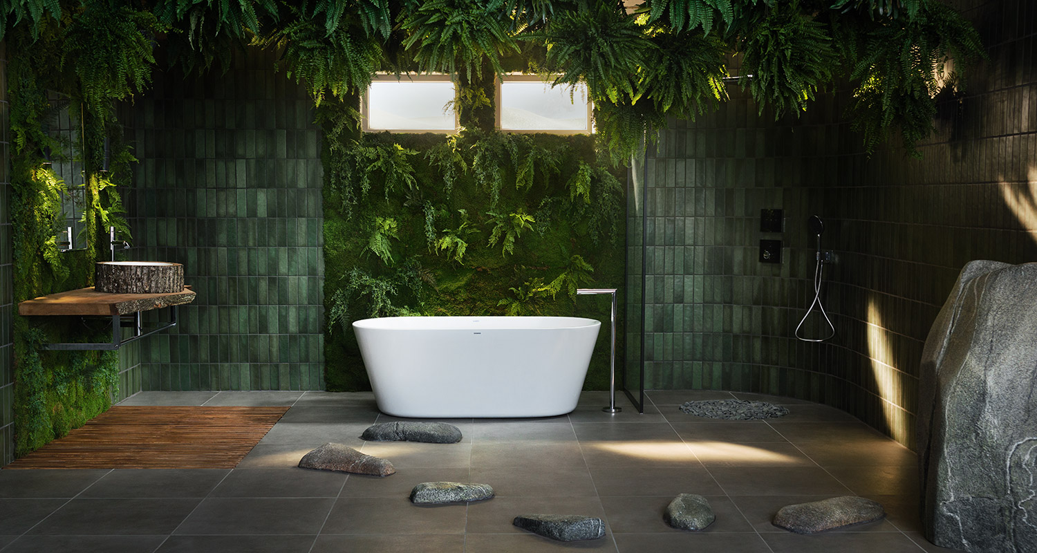 Valkoinen kylpyamme tummanvihreiden laattojen ja sammalseinän edessä, kivipolku ja puuallas.