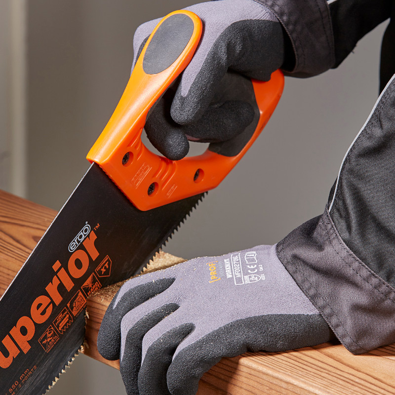 Harmaat työhanskat pitelevät oranssi-mustaa sahan kahvaa sahaten puulankkua.