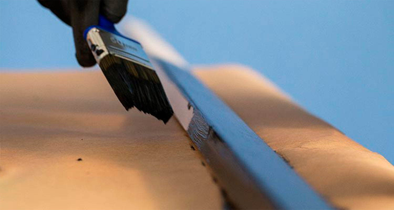 Mustahansikkainen käsi siveltelee sinivartisella siveltimellä mustaa maalia beigen reunaan.