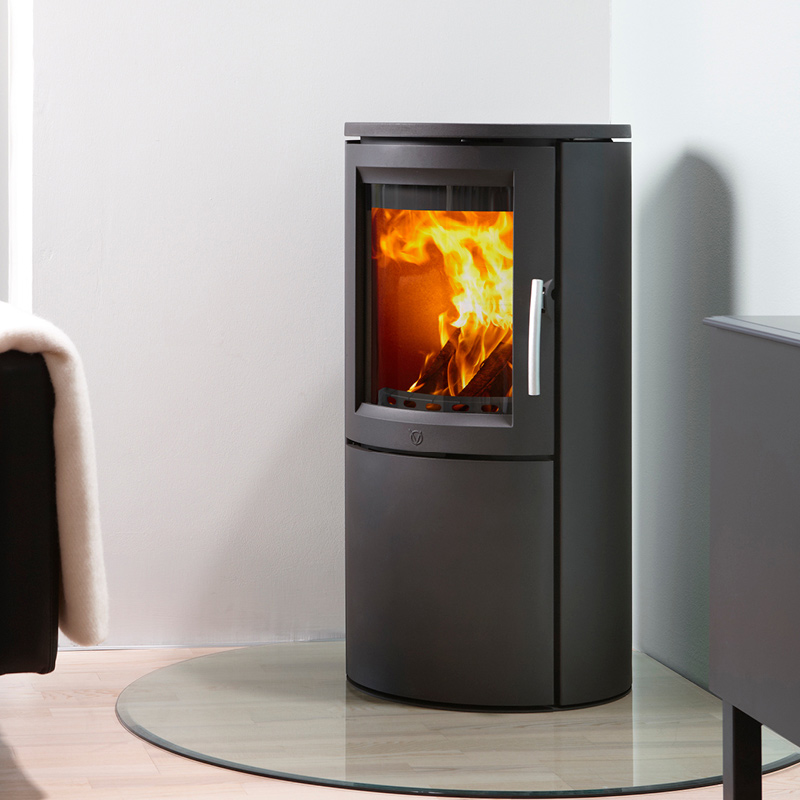 Musta pyöreä takka palaa oransseilla liekeillä vaaleassa olohuoneessa