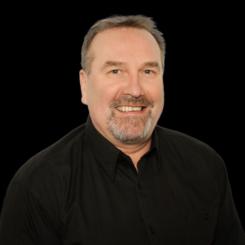 Harmaatukkainen mies mustassa kauluspaidassa mustalla taustalla.