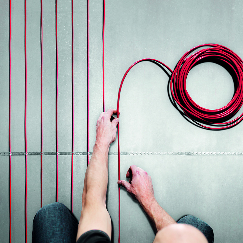 Ylhäältä kuvattu henkilö asettelee punaisia kaapeleita harmaalle lattialle.
