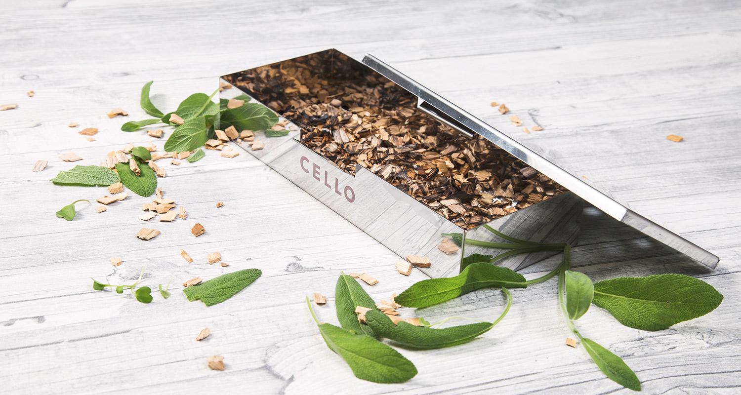 Hopeinen Cello-laatikko täynnä puukuituhaketta, tuoreita vihreitä salvianlehtiä vaalealla puupöydällä