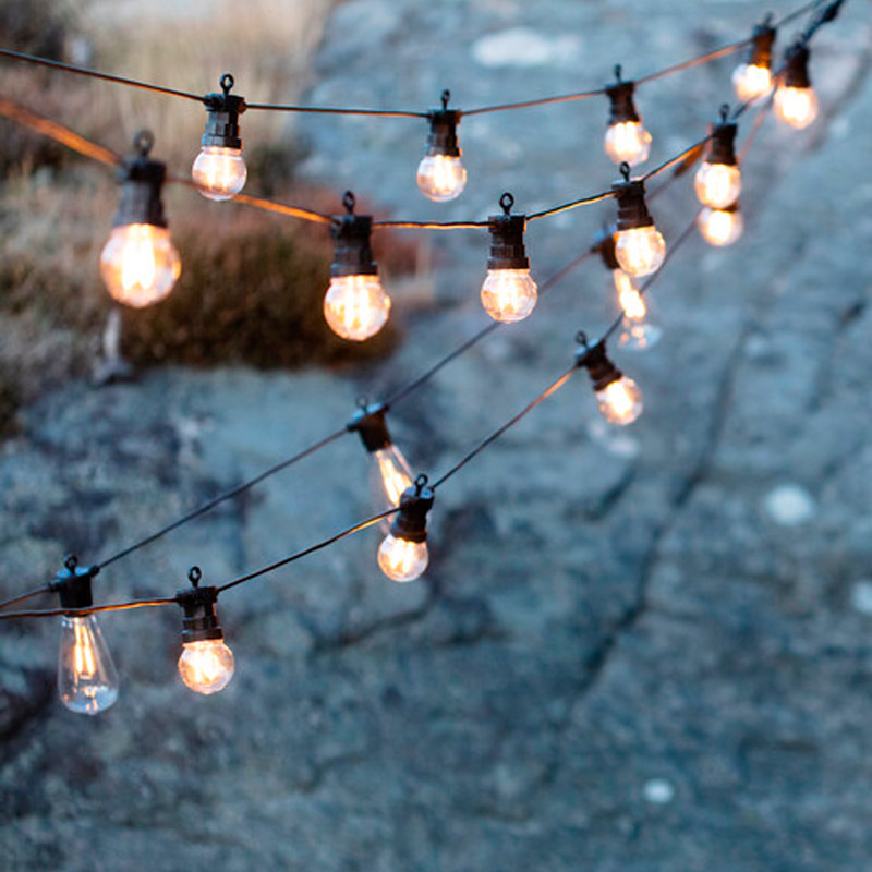 Kolmessa rivissä roikkuvia lämpimän keltaisia ulkovalaisimia kalliotaustalla.