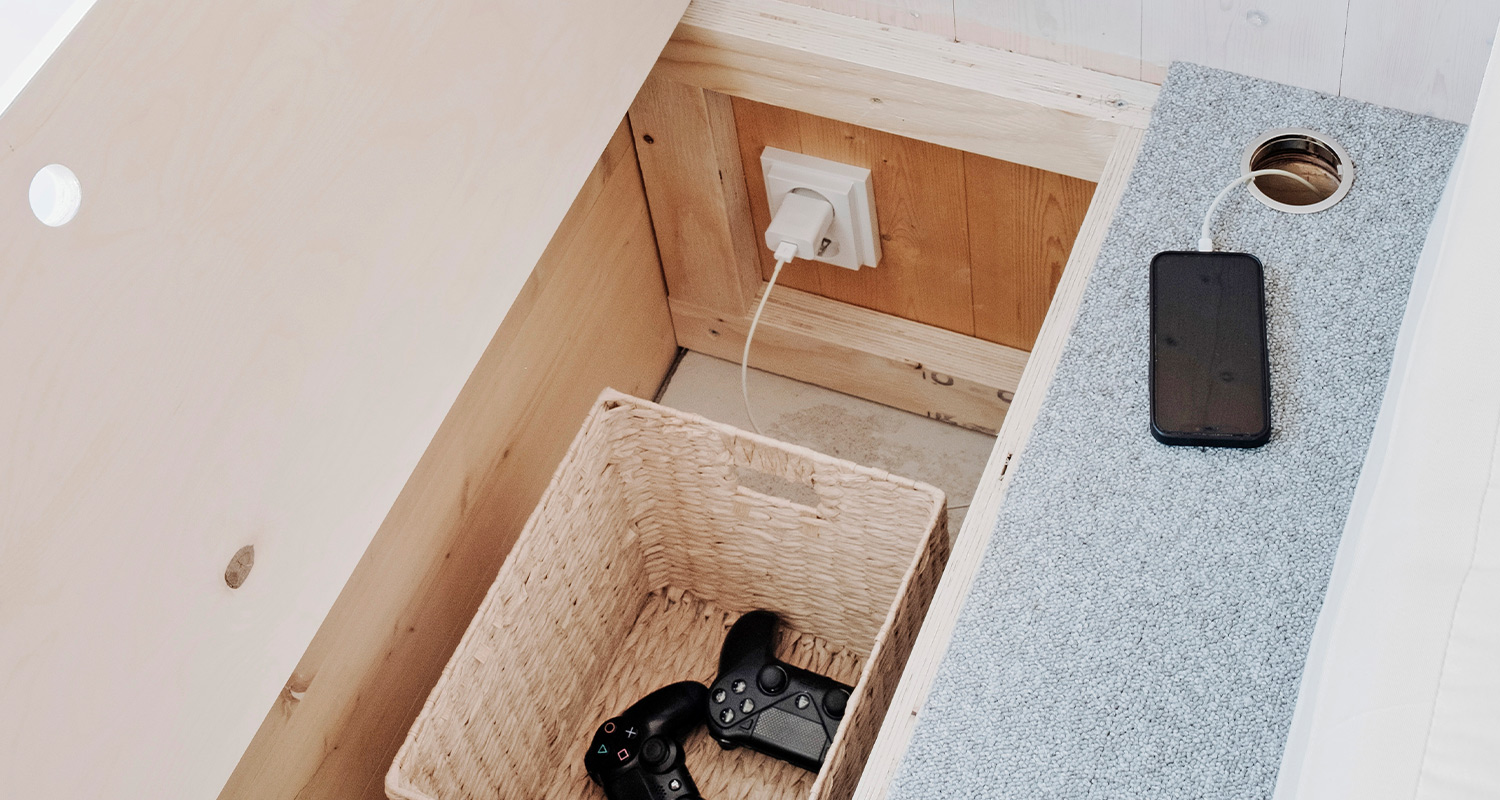 Korotettu alkovi, jossa pistorasiat sekä puhelimen ja peliohjaimien latausmahdollisuus.