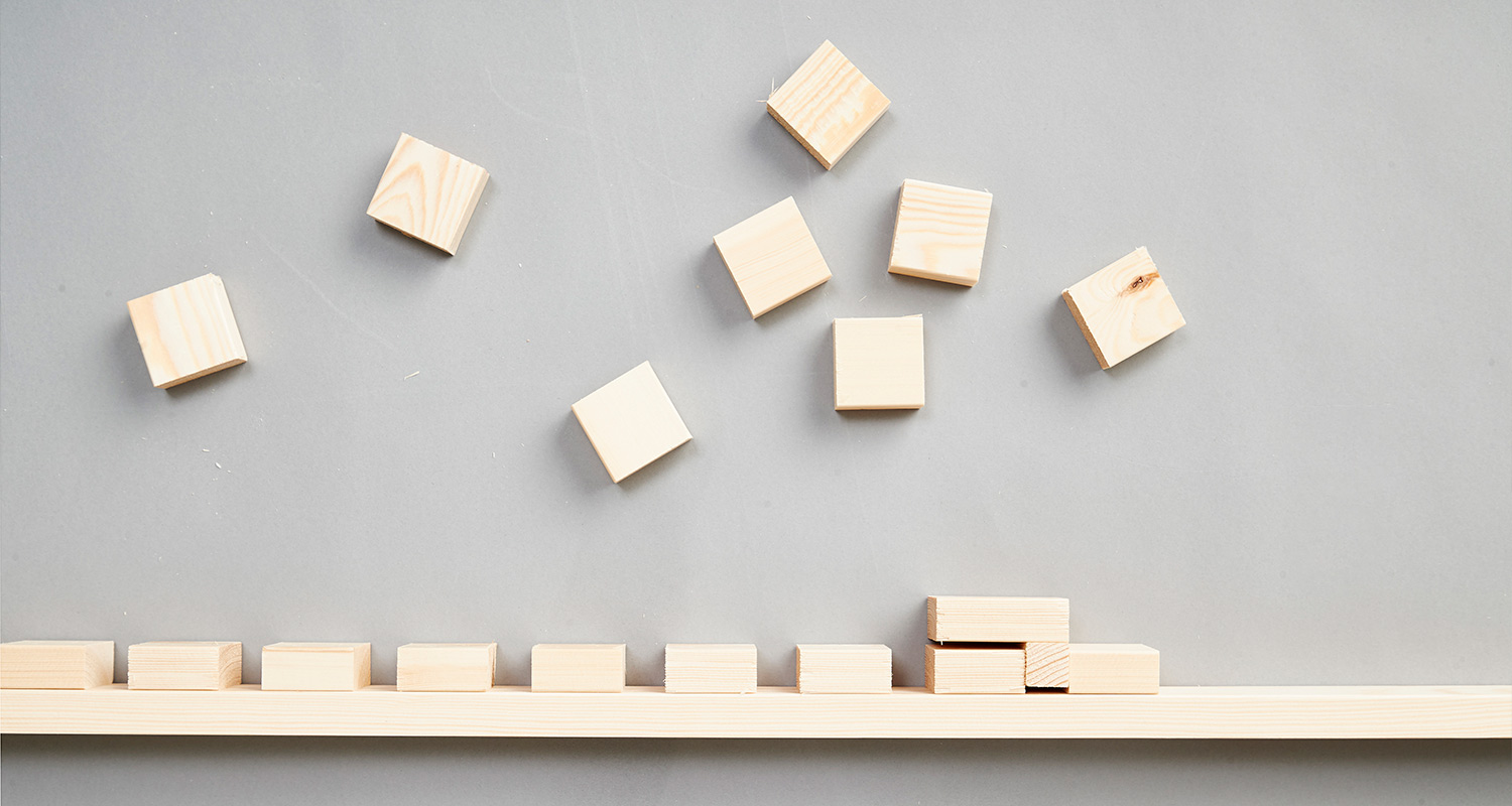 Harmaalla taustalla vaaleita puukuutioita, osa alarivin rivissä, osa hajallaan yläpuolella.