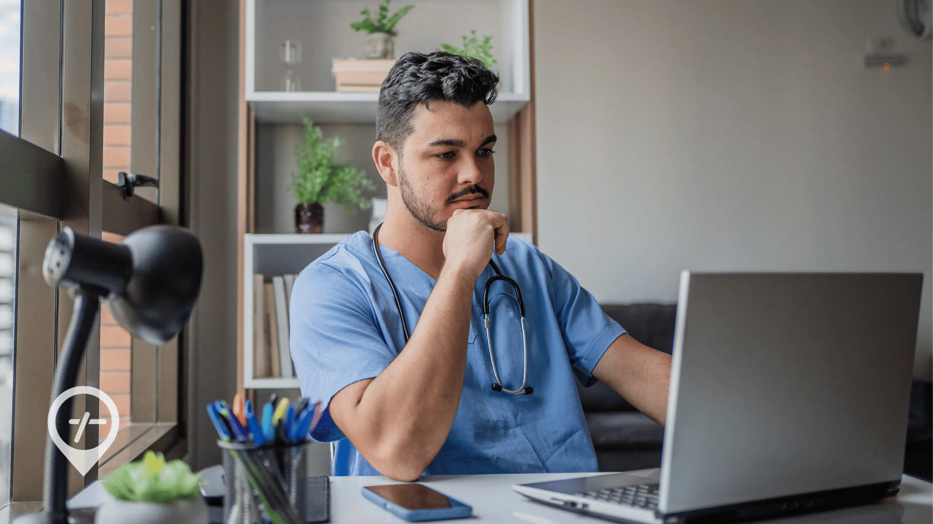 A nurse manager sits at his desk and looks at a computer.