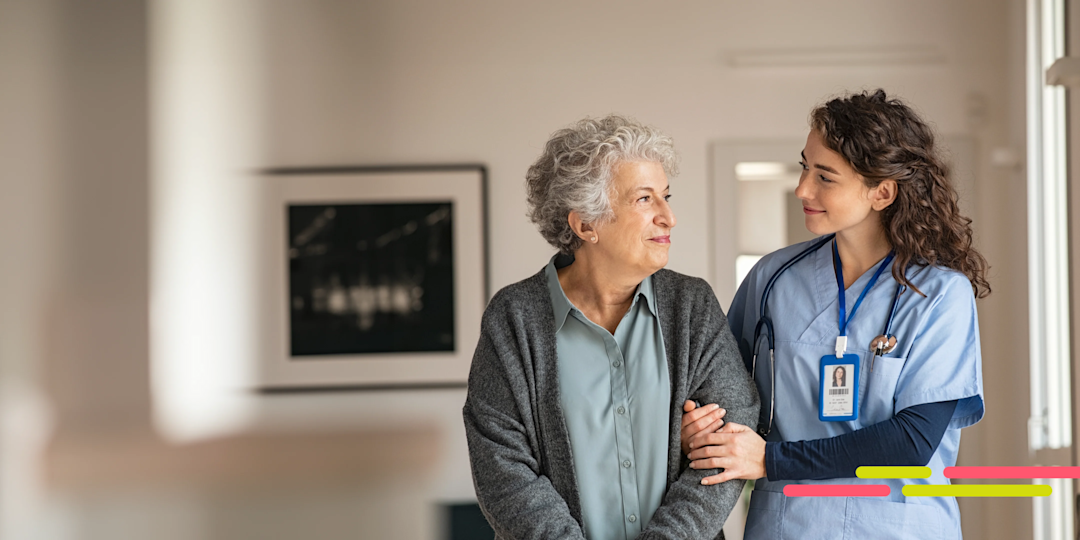 Nurse helping an elderly woman walk down a hallway.