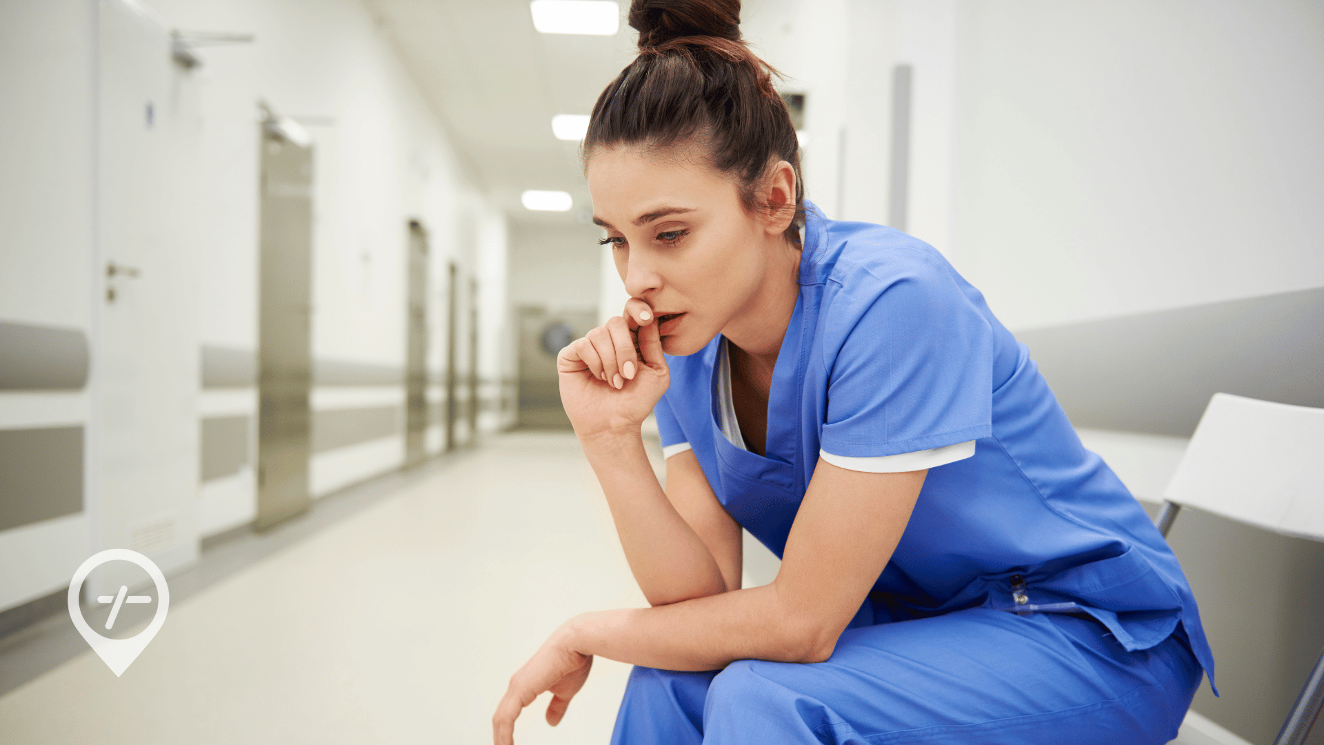 A visibly tired nurse sitting in a hospital hallway chair, pausing during a busy shift to convey the emotional and physical strain that can lead to nurse burnout.