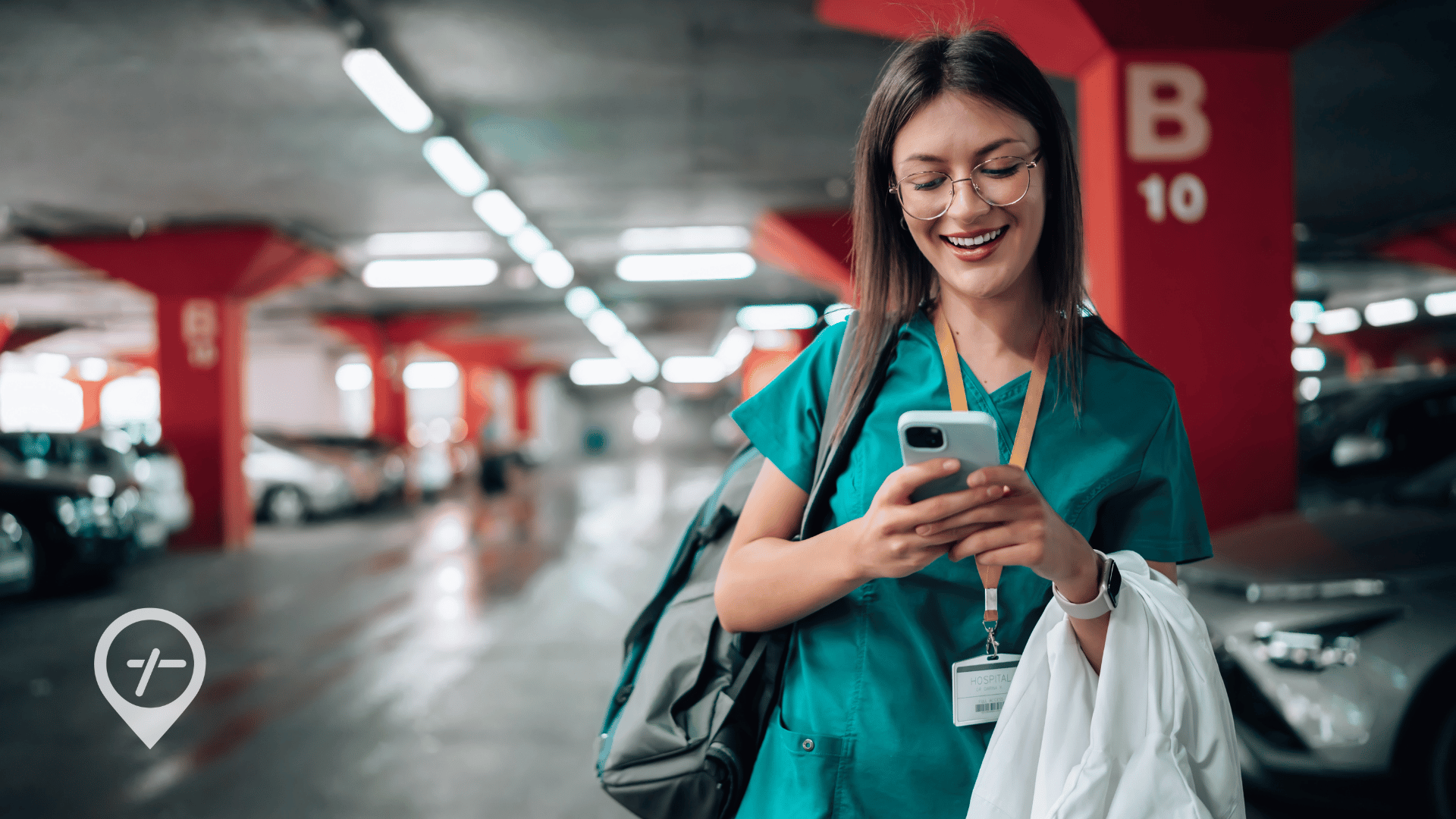 A nurse walks through a LTACH parking garage, smiling and looking at her phone. 