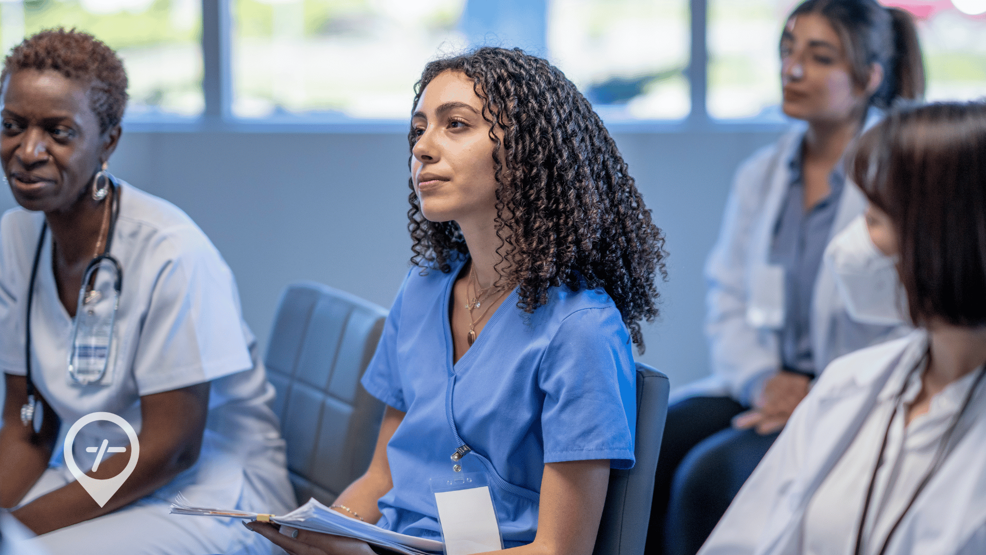 A nurse sitting in a hospital conference room with other healthcare professionals.