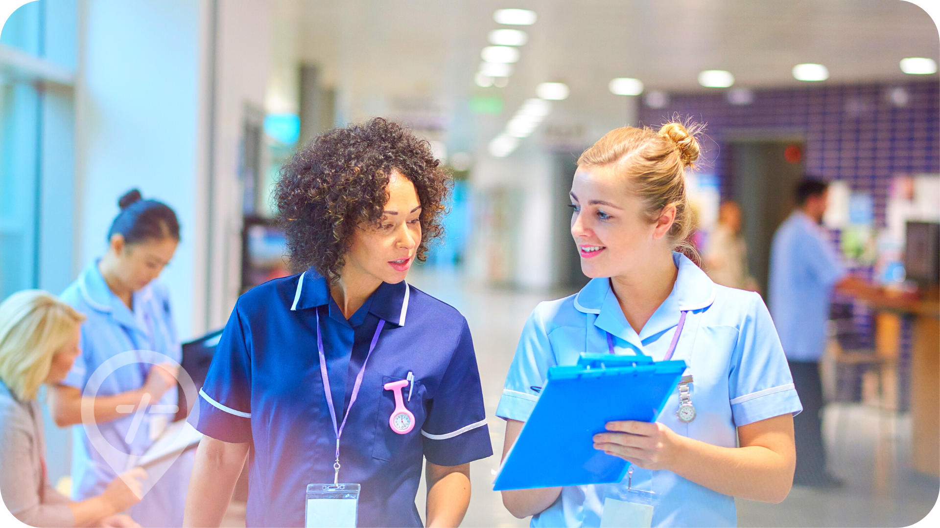 Two female nurses walk down hospital hallway.