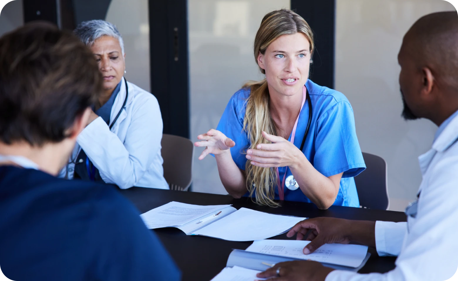 A female nurse is speaking to doctors during a healthcare team meeting.
