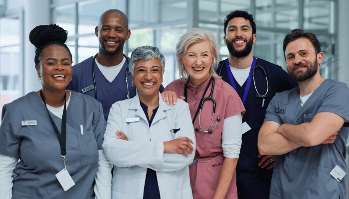 A group of nurses from different generations stand next to a doctor in a hospital hallway. 