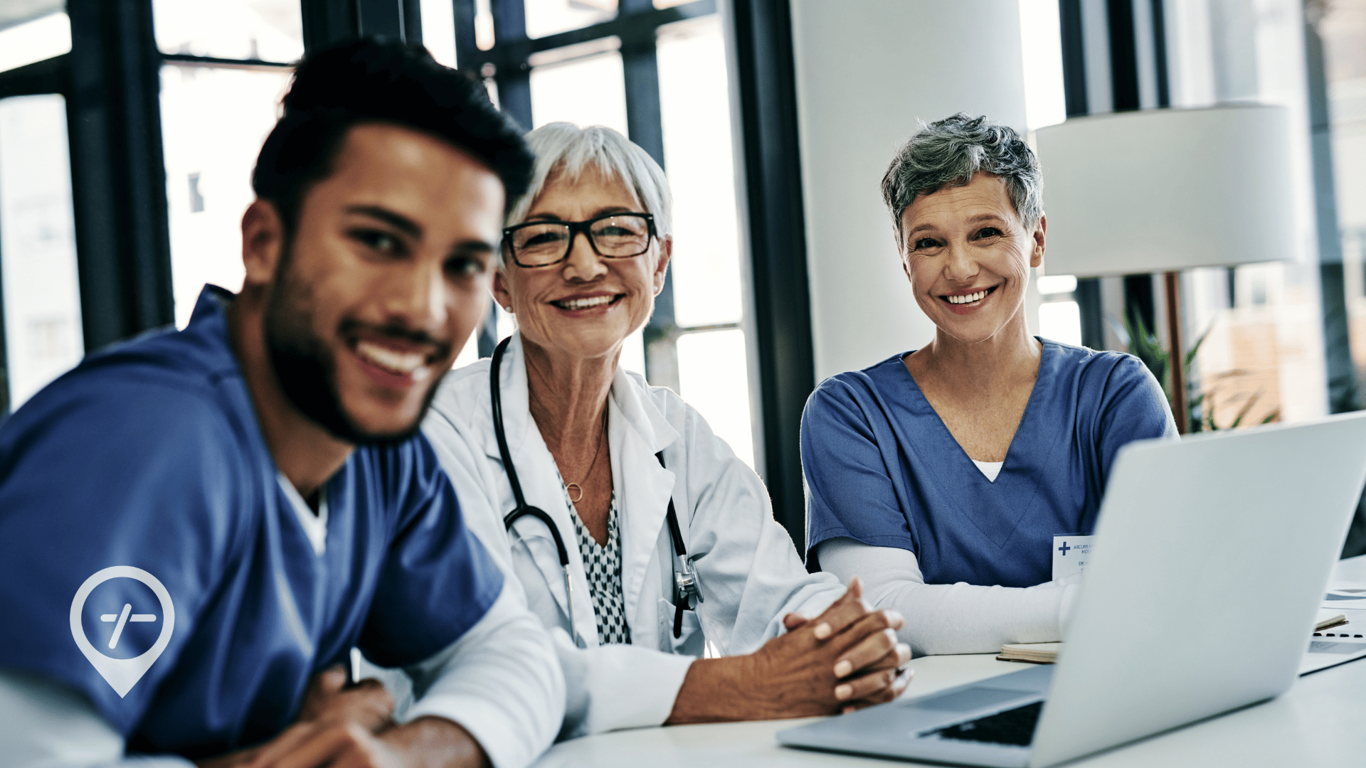 A multigenerational clinical team sitting at a computer desk and smiling at the camera.