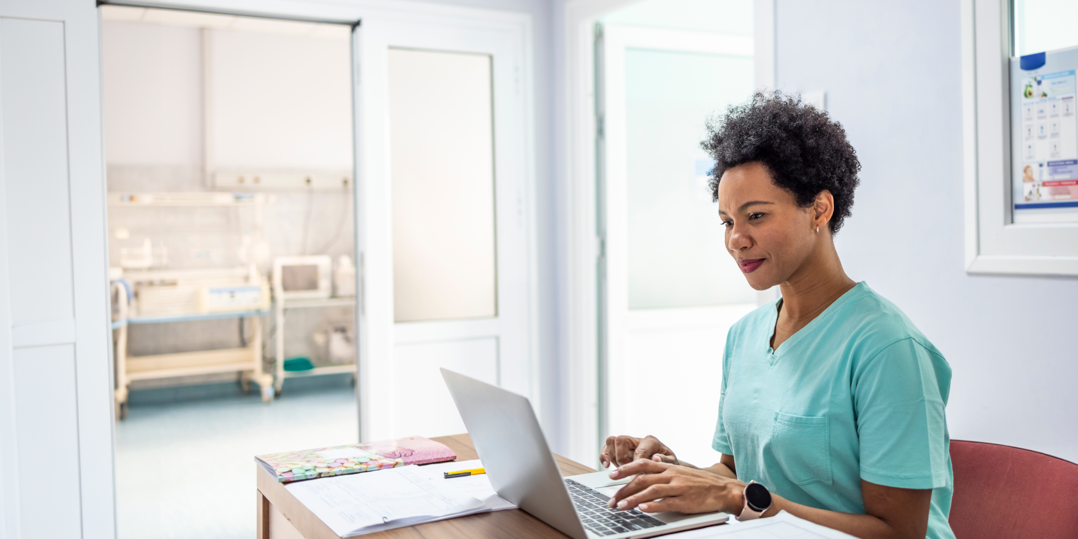 African American nurse in scrubs working on laptop computer.