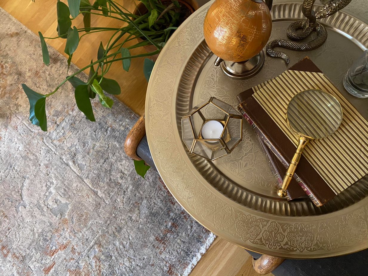 Golden serving plate with following items: globe, candle, books and a magnifying glass. 