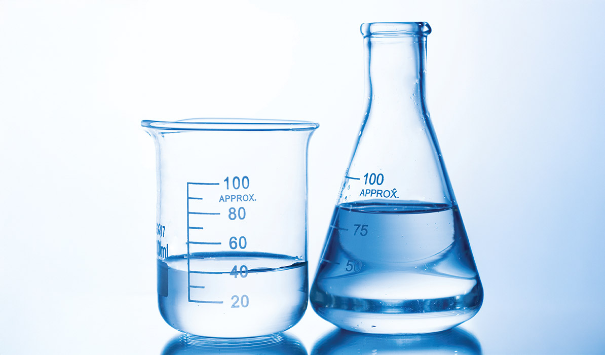 Laboratory glassware including beakers and a flask filled with clear liquid on a reflective surface.