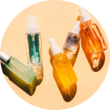 Assorted skincare oils in glass dropper bottles arranged on a circular surface, showcasing different colors and textures.