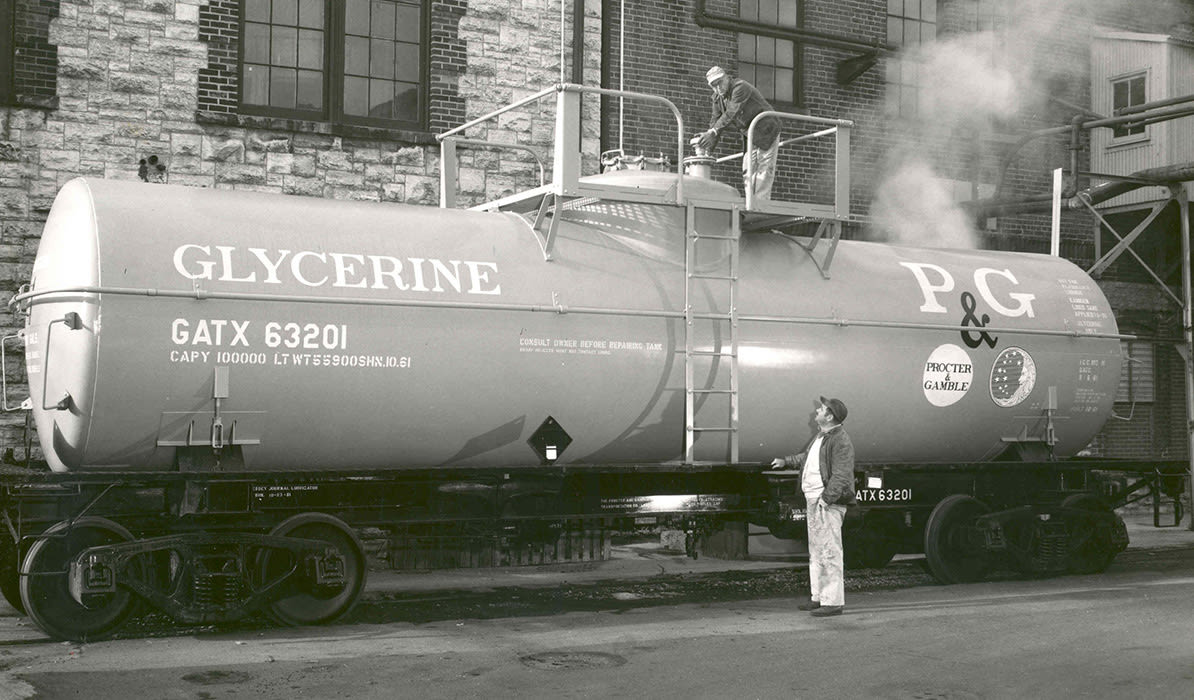 Black-and-white image of a historic PG glycerine tanker with a man standing beside it.