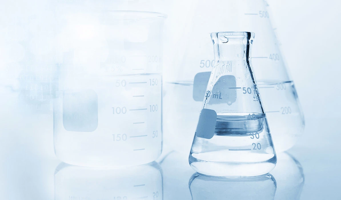 Laboratory glassware including beakers and a flask filled with clear liquid on a reflective surface.