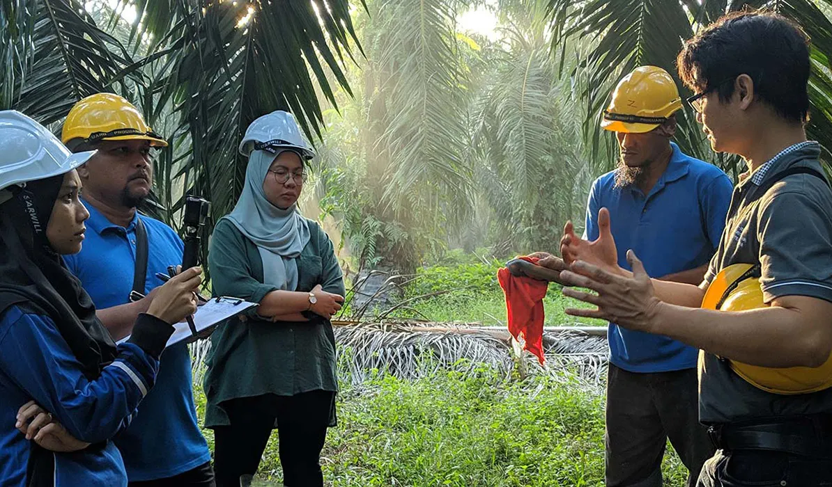 Group of people in helmets engaged in a discussion outdoors surrounded by palm trees and greenery.