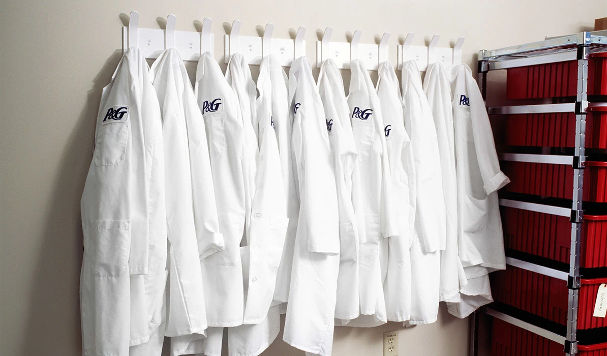 A row of white lab coats hanging on hooks inside a laboratory or research facility.