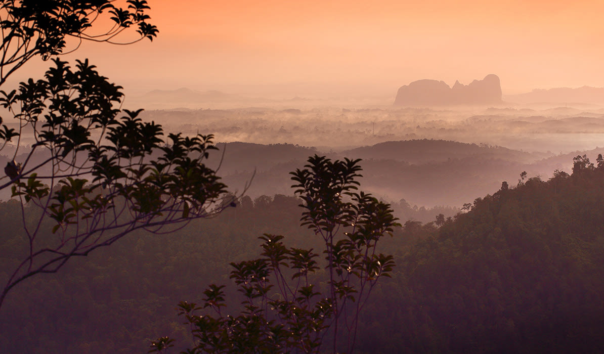 Scenic view of misty hills at sunrise with silhouette of mountains in the background showing vibrant colors of dawn.