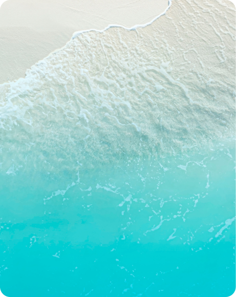 Aerial view of a sandy beach with gentle waves lapping at the shore, featuring clear turquoise water and white sand.