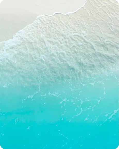 Aerial view of a sandy beach with gentle waves lapping at the shore, featuring clear turquoise water and white sand.