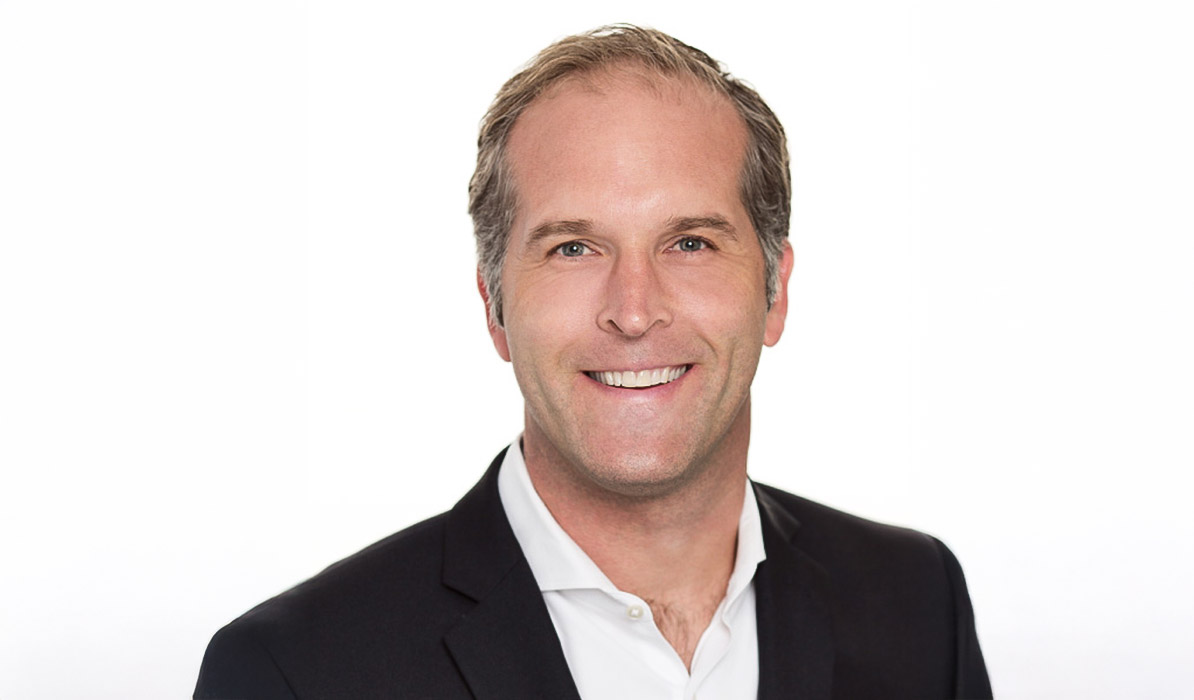 Smiling man with short hair, wearing a black blazer and white shirt, on a white background.