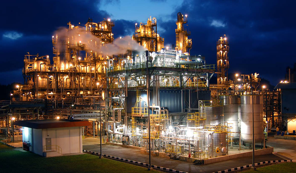 Large industrial plant illuminated at night, with smoke rising from the facility.