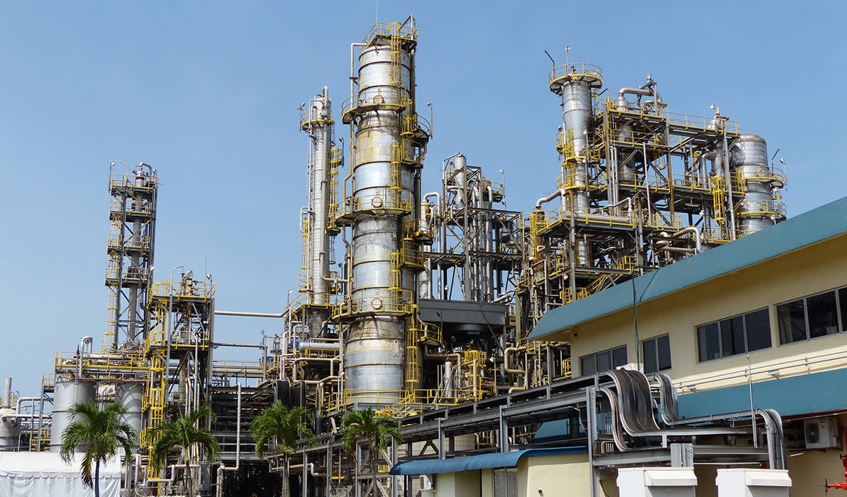 Industrial complex with numerous large pipes, towers, and tanks against a clear blue sky.