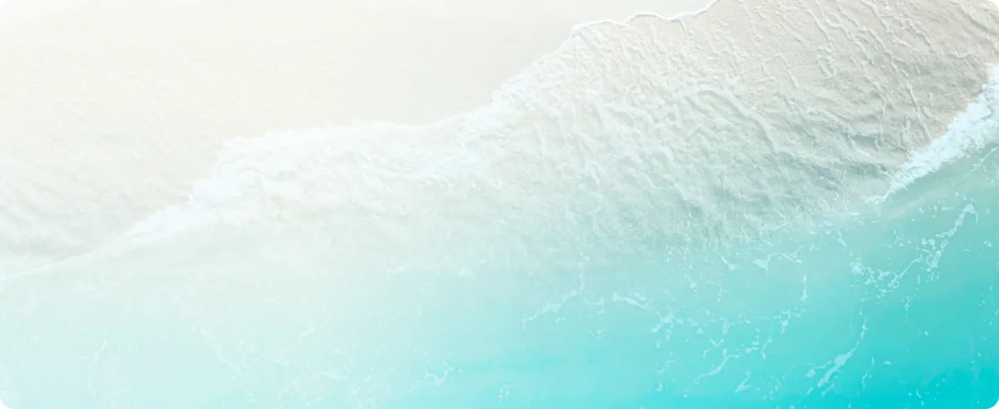  Aerial view of a sandy beach with gentle waves lapping at the shore, featuring clear turquoise water and white sand.