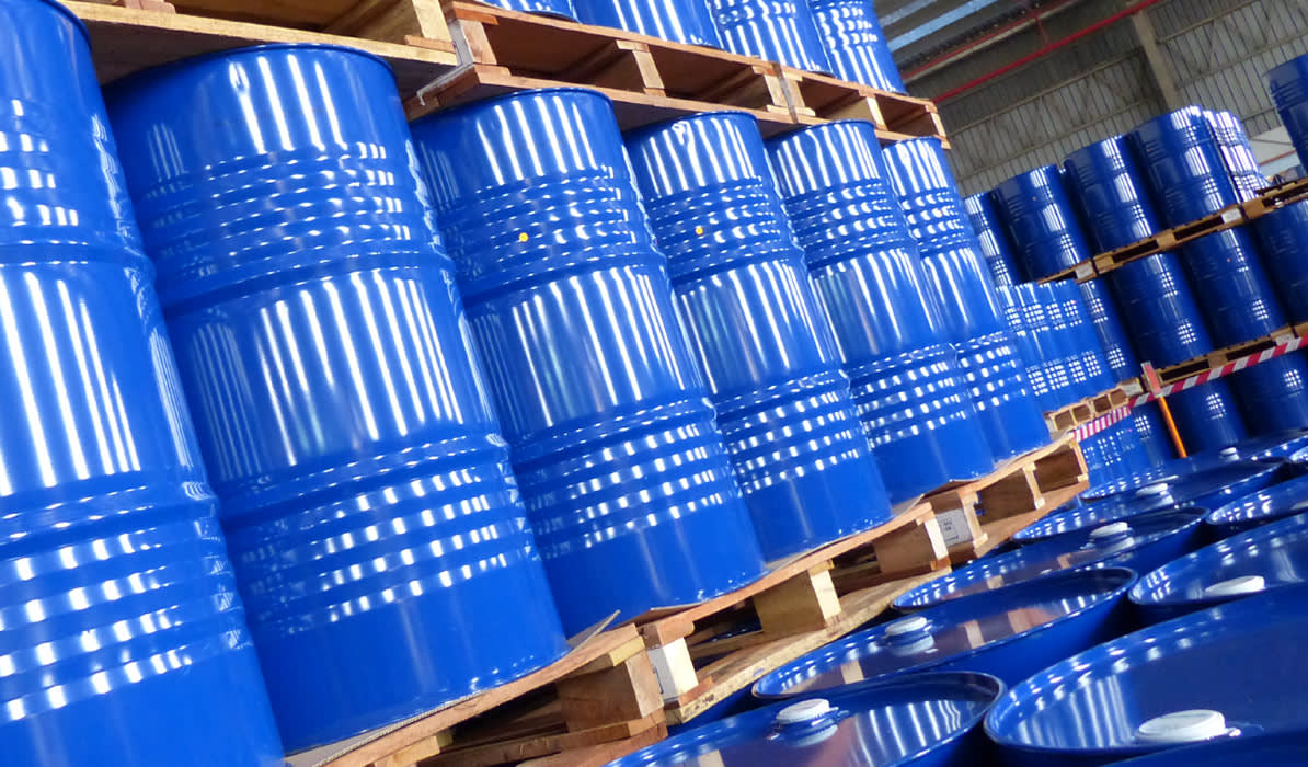 Stacks of shiny blue barrels stored on wooden pallets in a warehouse, with some barrels visible in the foreground.