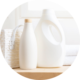  Bottles of laundry detergent and fabric softener on a wooden surface with towels and a basket in the background.